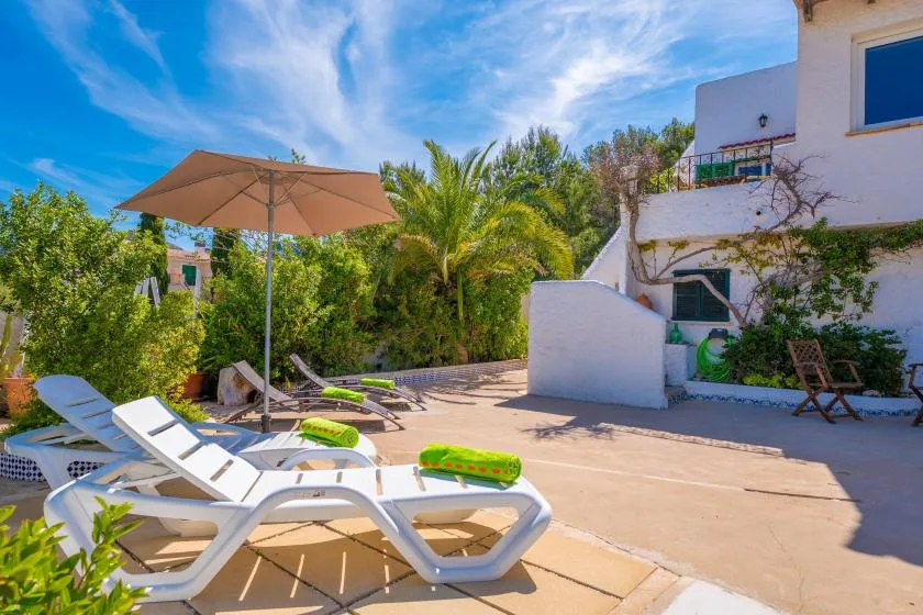 A sunny outdoor patio with lounge seating, an umbrella, and leafy greenery.