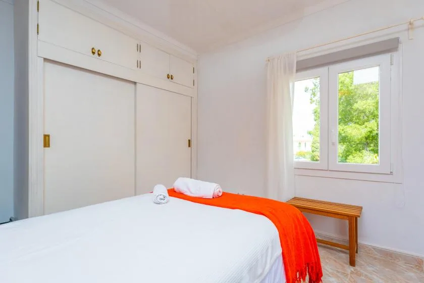 A bedroom with a white bed and a bright orange throw beside a window.