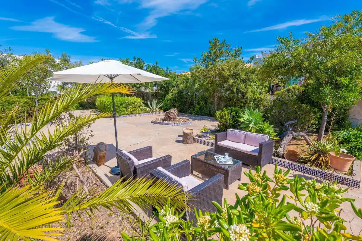 An outdoor patio with seating, a large umbrella, and surrounding greenery.