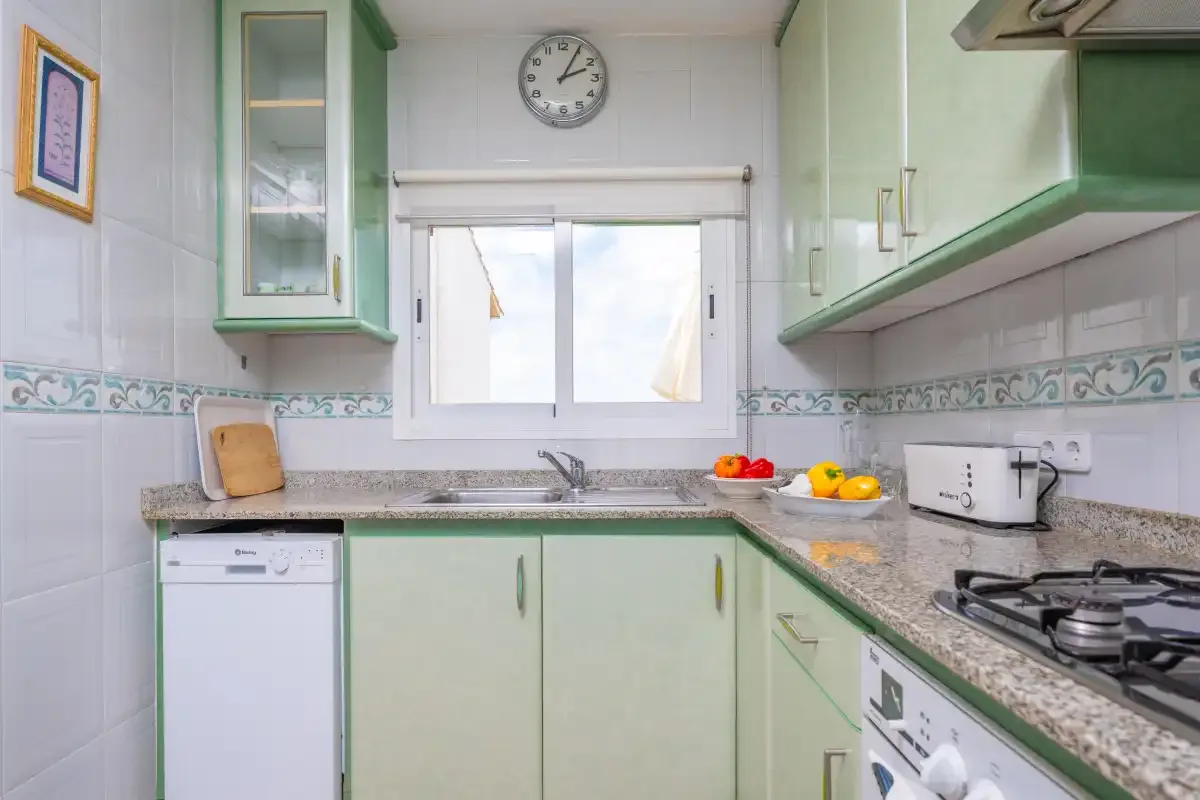 A bright kitchen with green cabinets, a countertop, and a window above the sink.