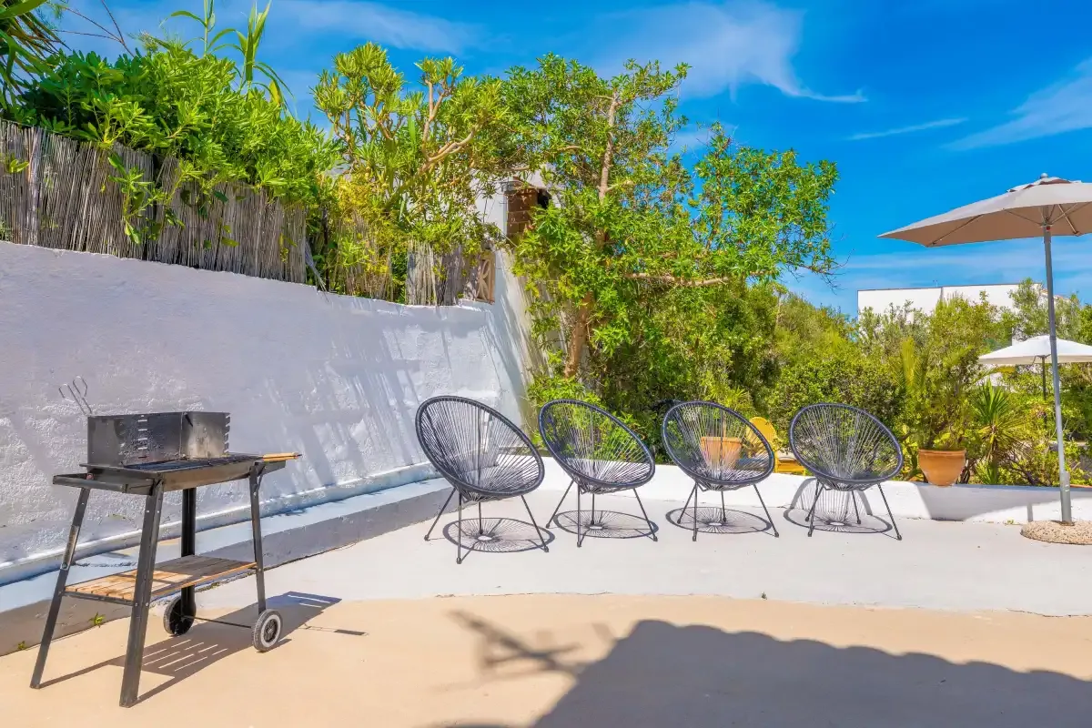 A sunny outdoor patio with a barbecue, seating, and a large umbrella.