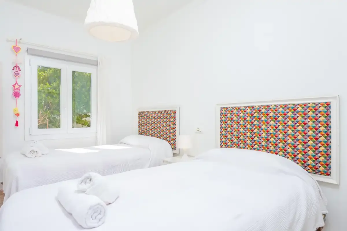 A bright bedroom with two beds and colorful patterned headboards.