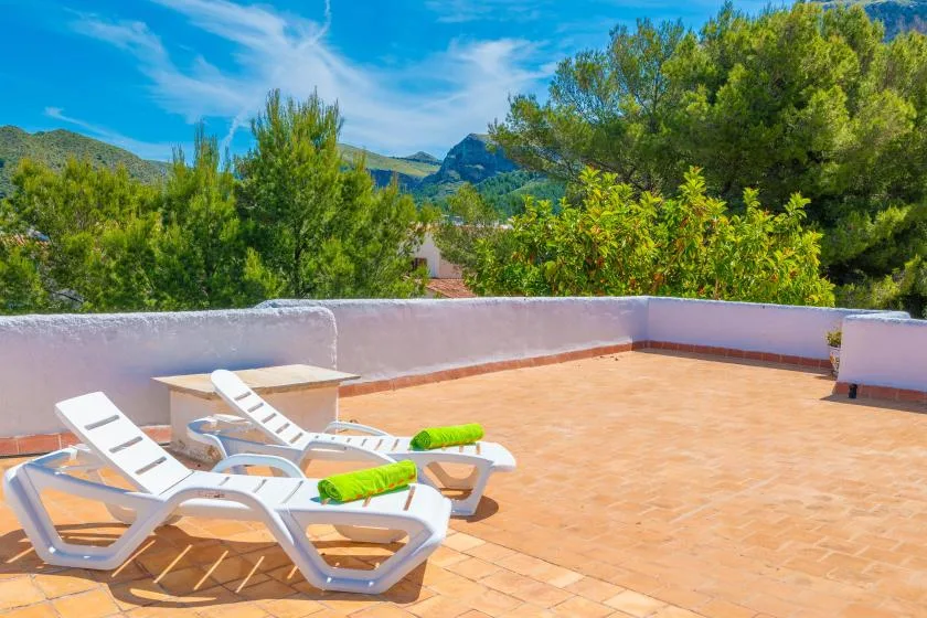 A sunny outdoor terrace has tiled flooring, lounge seating, and surrounding trees.