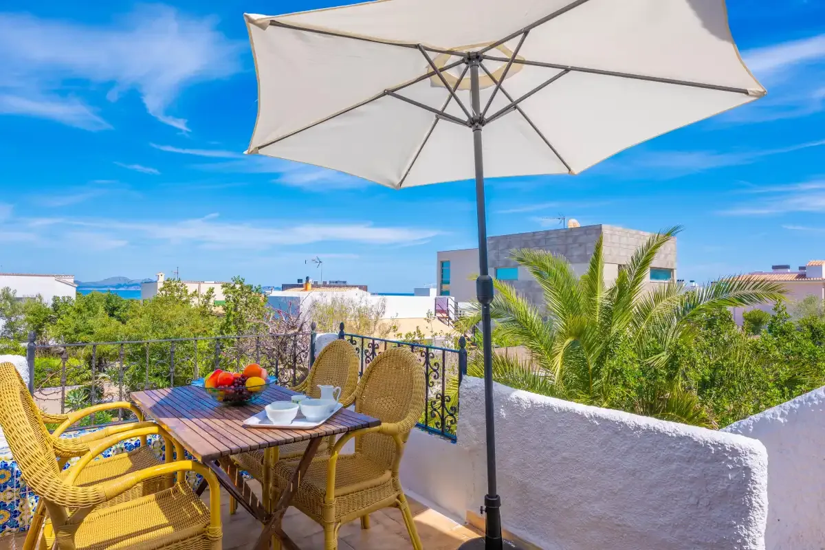 An outdoor terrace has wicker seating, a dining table, and a large sun umbrella.