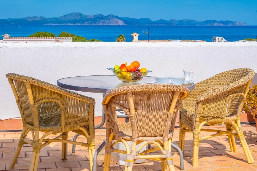 Outdoor dining table with wicker seating overlooks the sea.