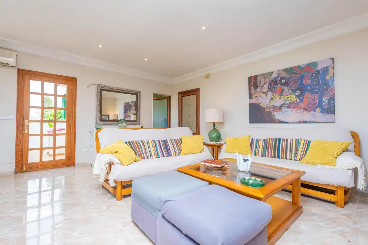 A bright living room with white seating, colorful cushions, and a wooden coffee table.