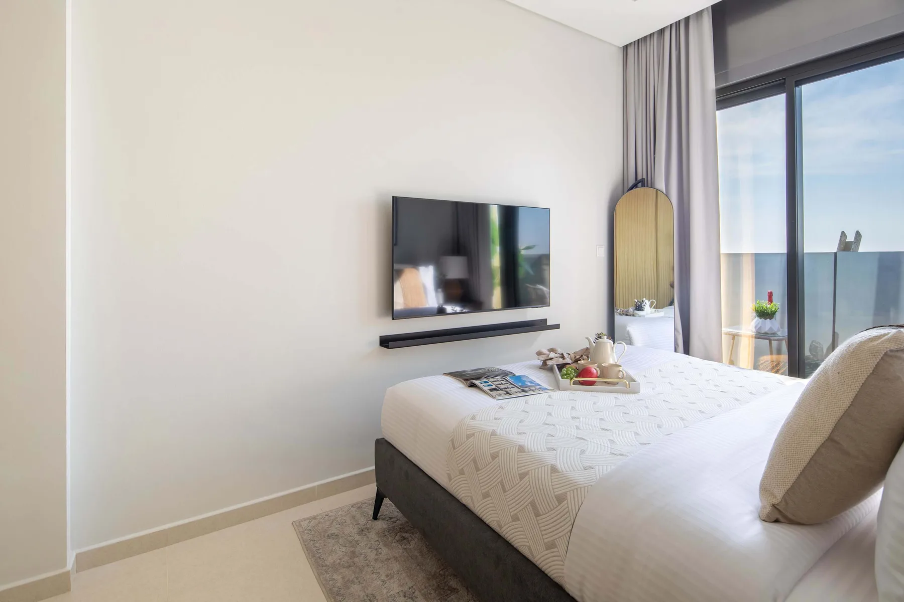 Un dormitorio luminoso con una cama, un televisor en la pared y ventanas grandes.