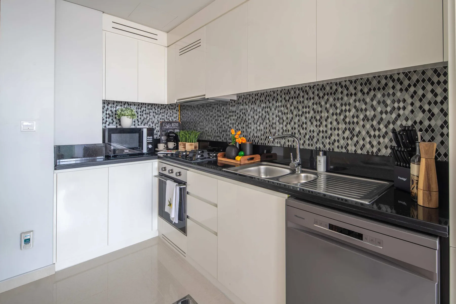 Una cocina moderna con gabinetes blancos, encimeras oscuras y un salpicadero estampado.