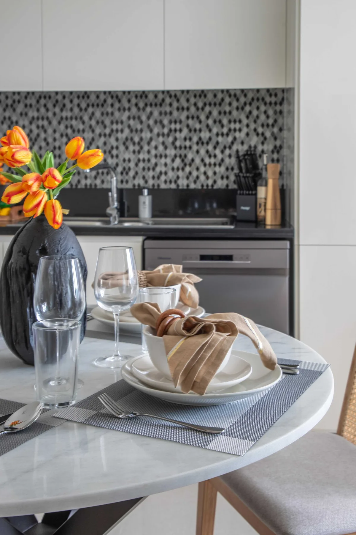 Una mesa de comedor con platos y vasos está frente a una cocina moderna.