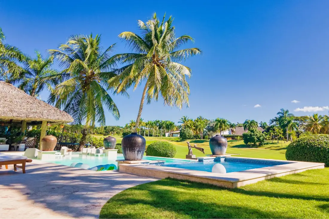 Una piscina está junto a un césped verde y palmeras.