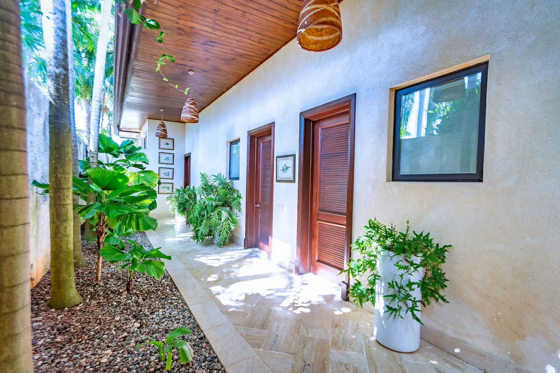 Un pasillo exterior cubierto con puertas de madera, una ventana y plantas en macetas.