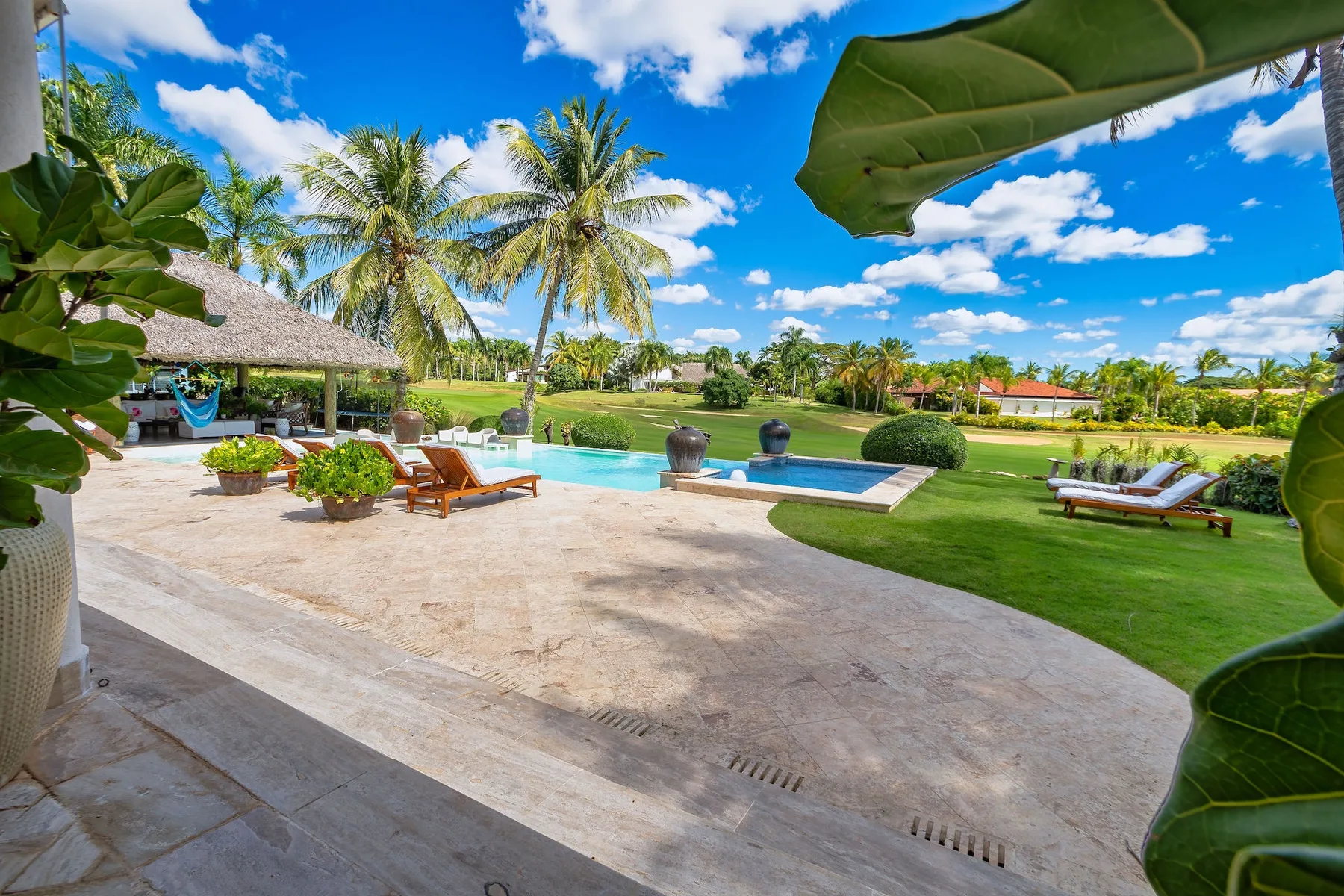 Una piscina tropical al aire libre junto a un patio pavimentado y palmeras.