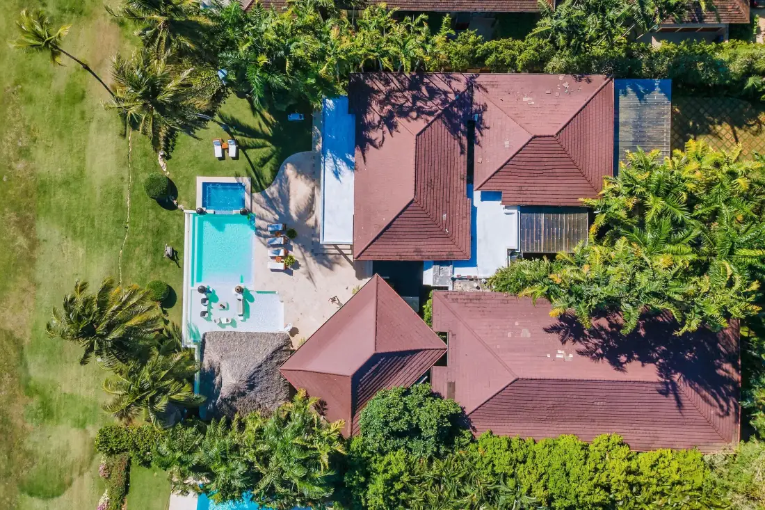 Vista aérea de una piscina junto a varios edificios de tejados rojizos y vegetación.