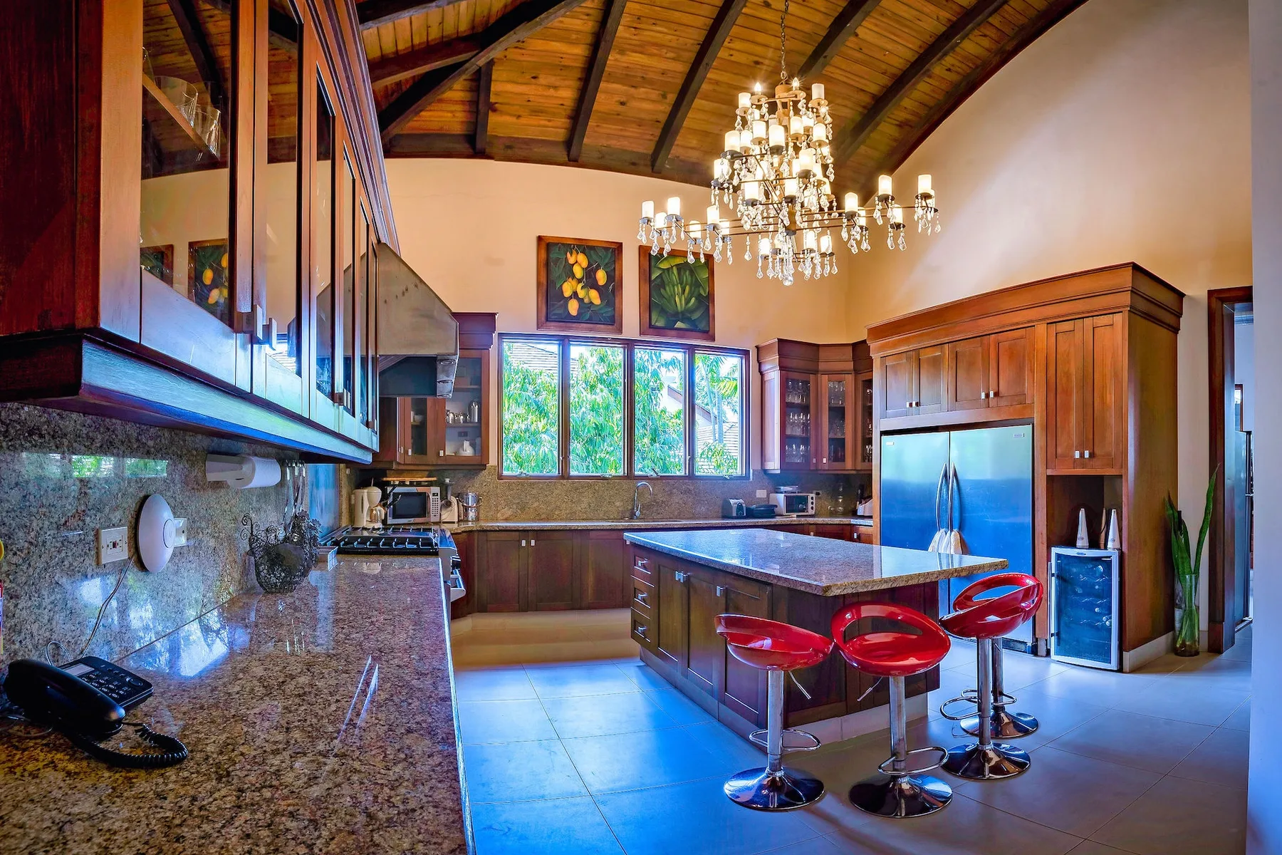 Una cocina amplia con gabinetes de madera oscura, una isla central y taburetes rojos.