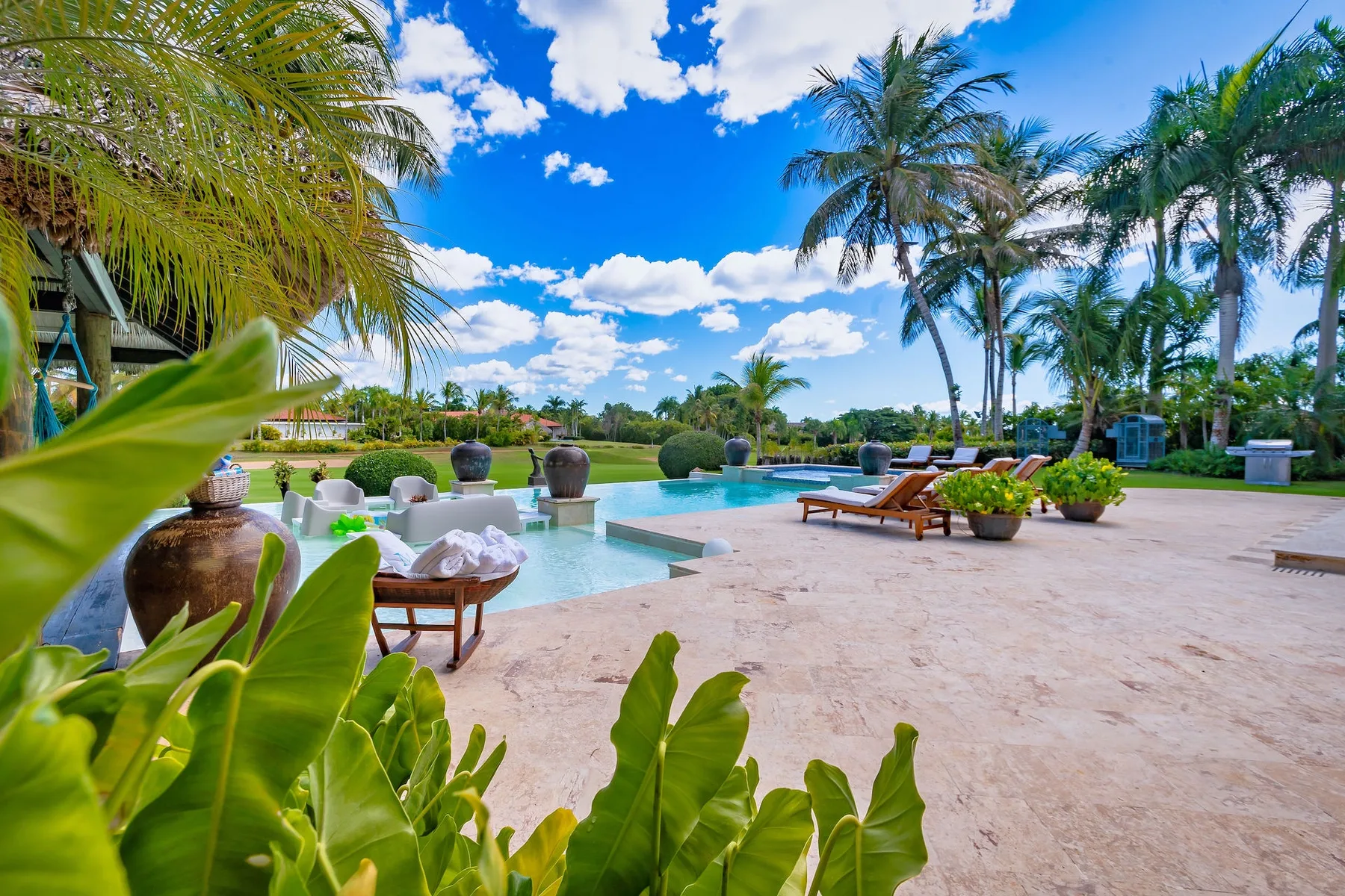 Un patio tropical junto a la piscina, con asientos y palmeras.