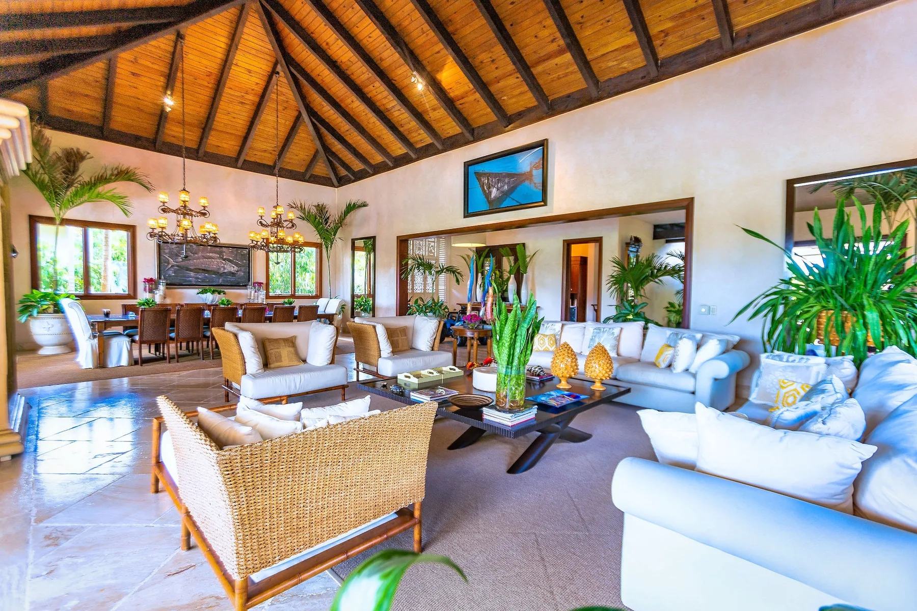 Una amplia sala de estar con asientos claros, plantas y un techo alto de madera.