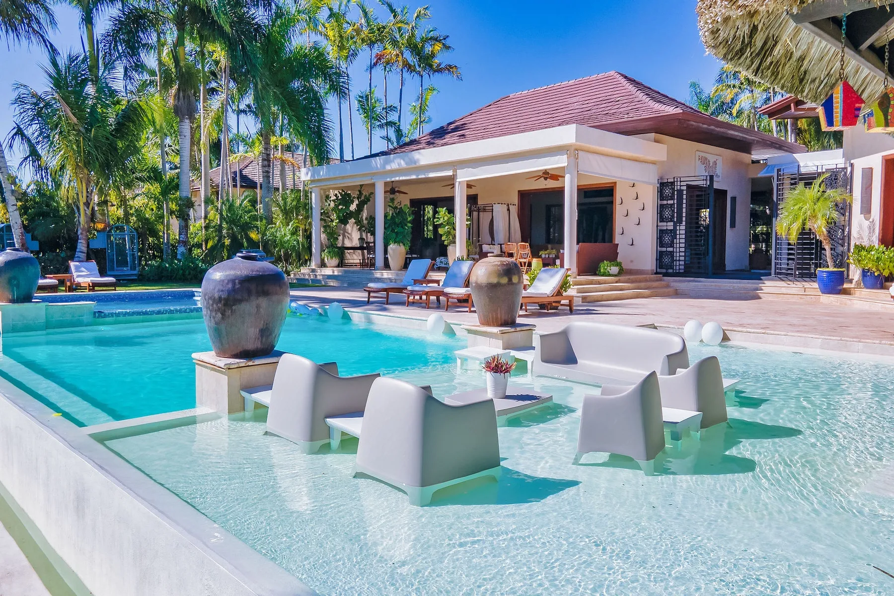 Una piscina tropical junto a un patio cubierto y asientos de descanso.