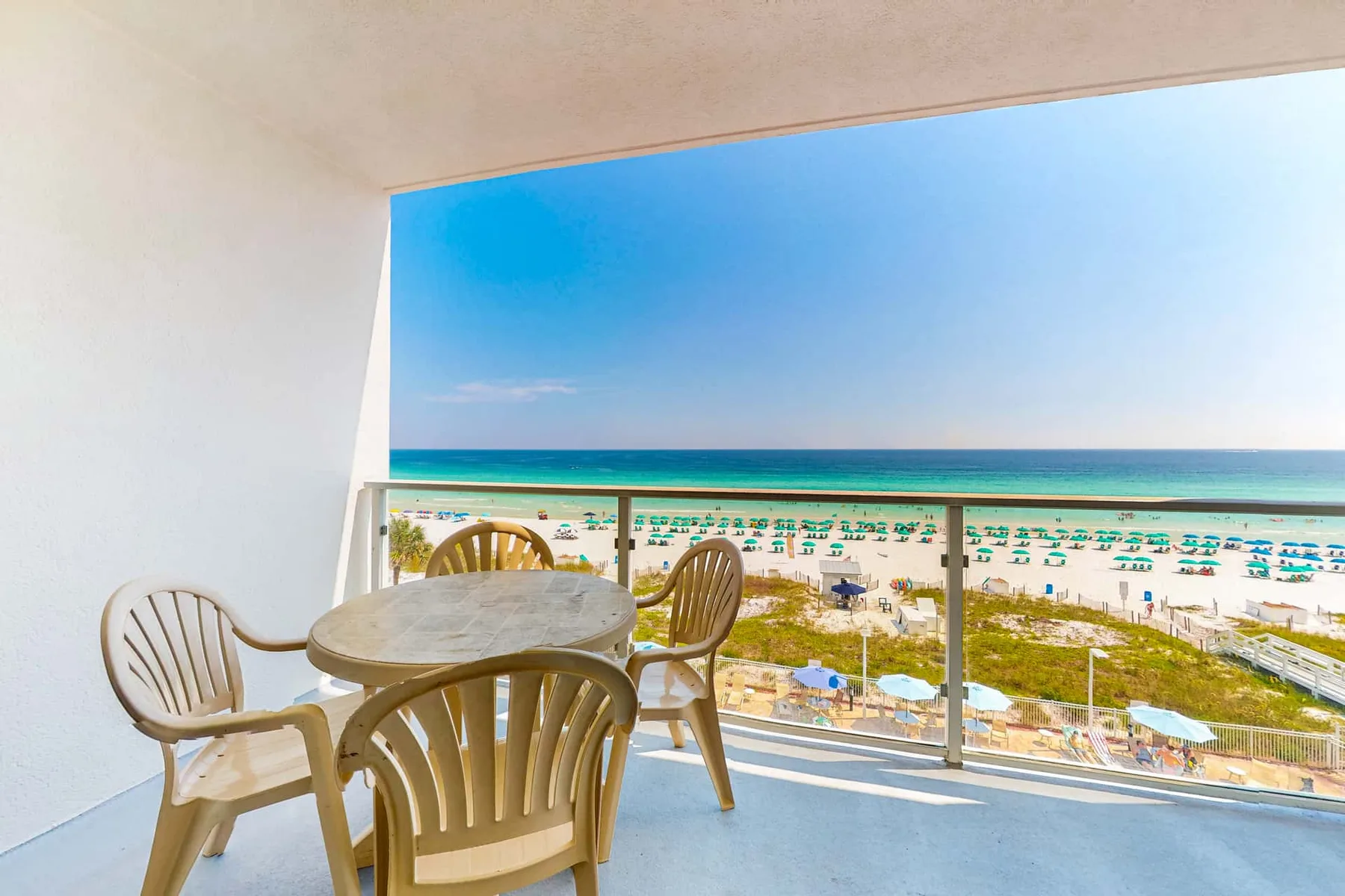 A balcony seating area overlooks a beach lined with umbrellas and the ocean.
