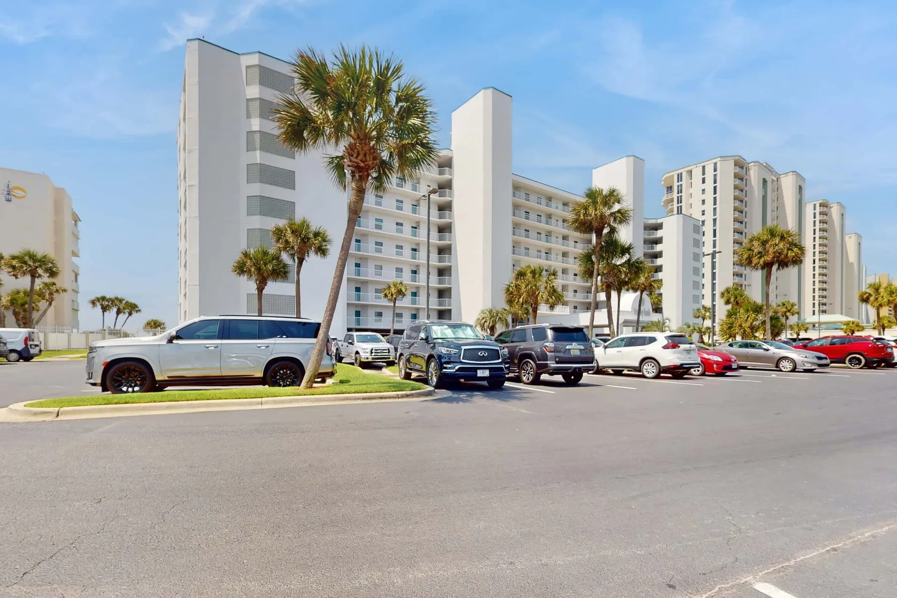 A high-rise building stands behind a parking lot lined with palm trees.