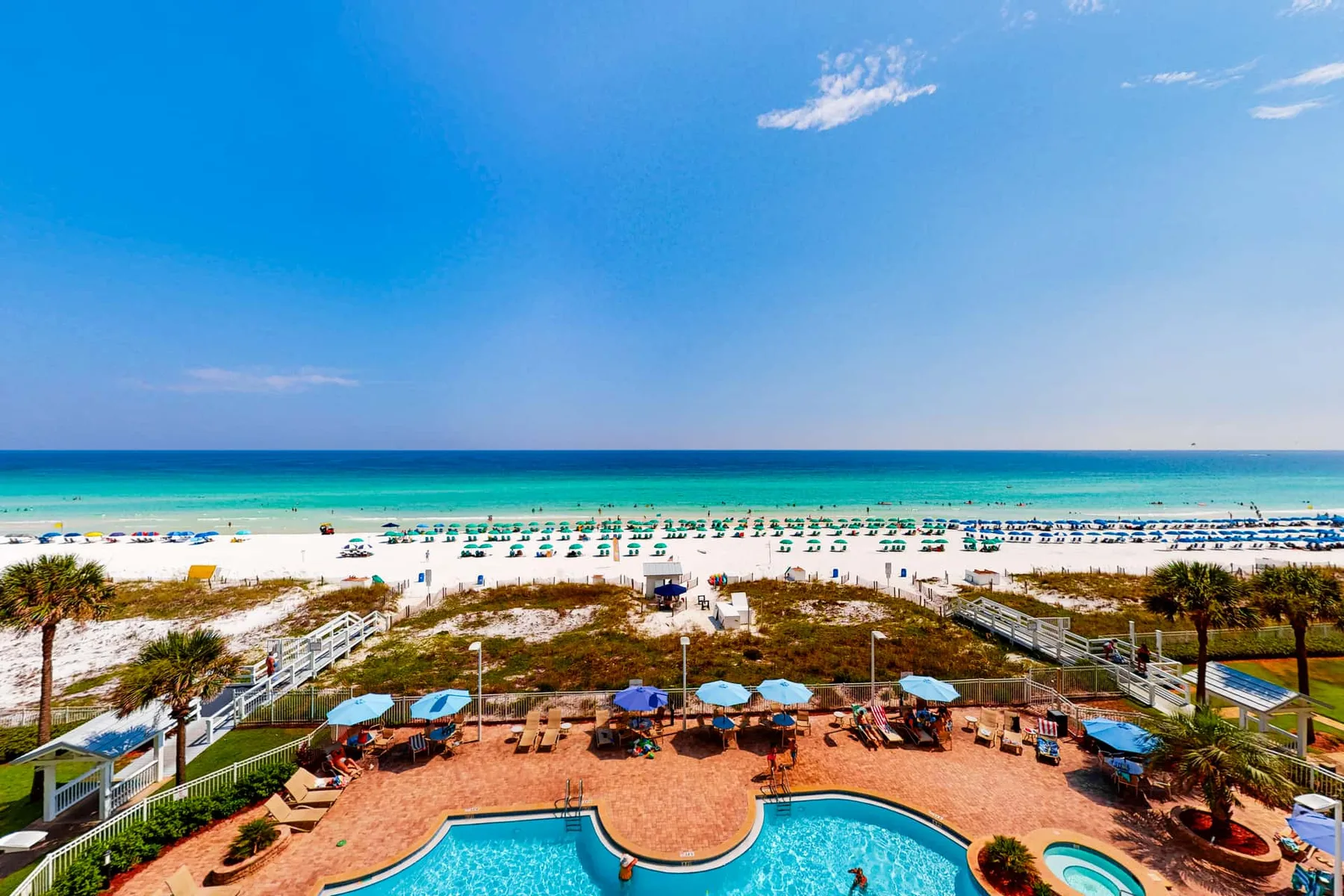 A beachside pool area faces a sandy beach and turquoise sea.