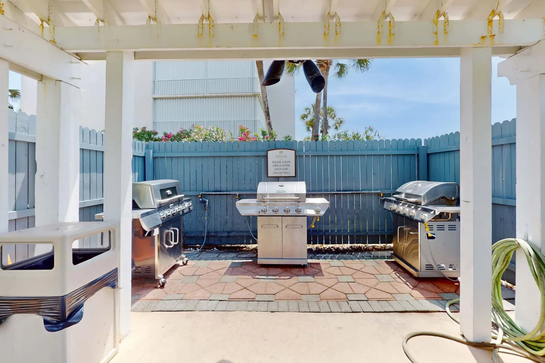 An outdoor grilling area with three grills beneath a white pergola.