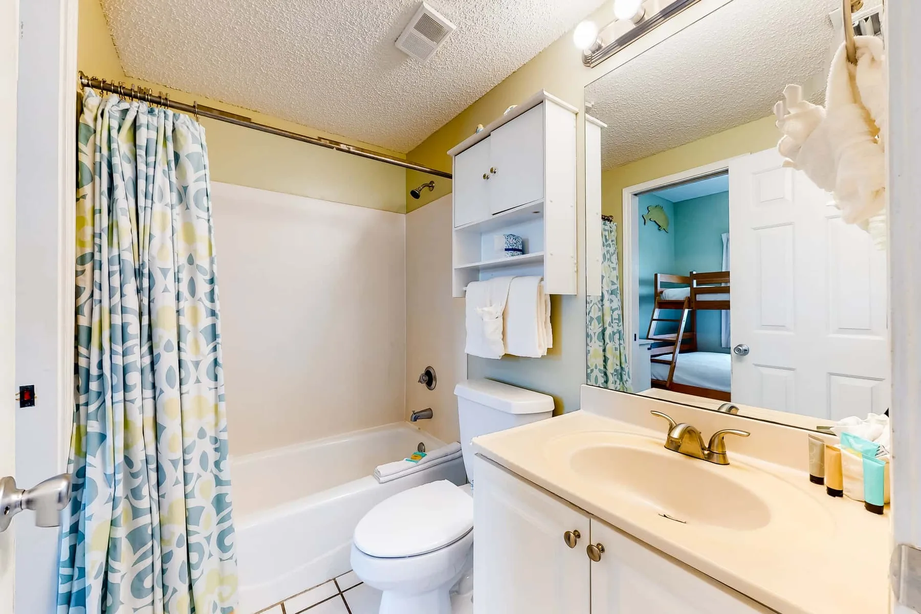 A bathroom with a bathtub, toilet, and sink beneath a large mirror.