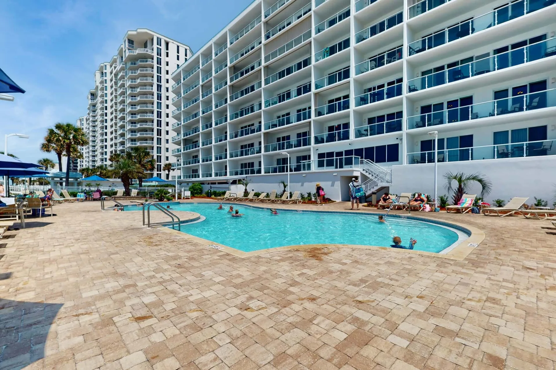 An outdoor swimming pool sits beside a large multi-story building.