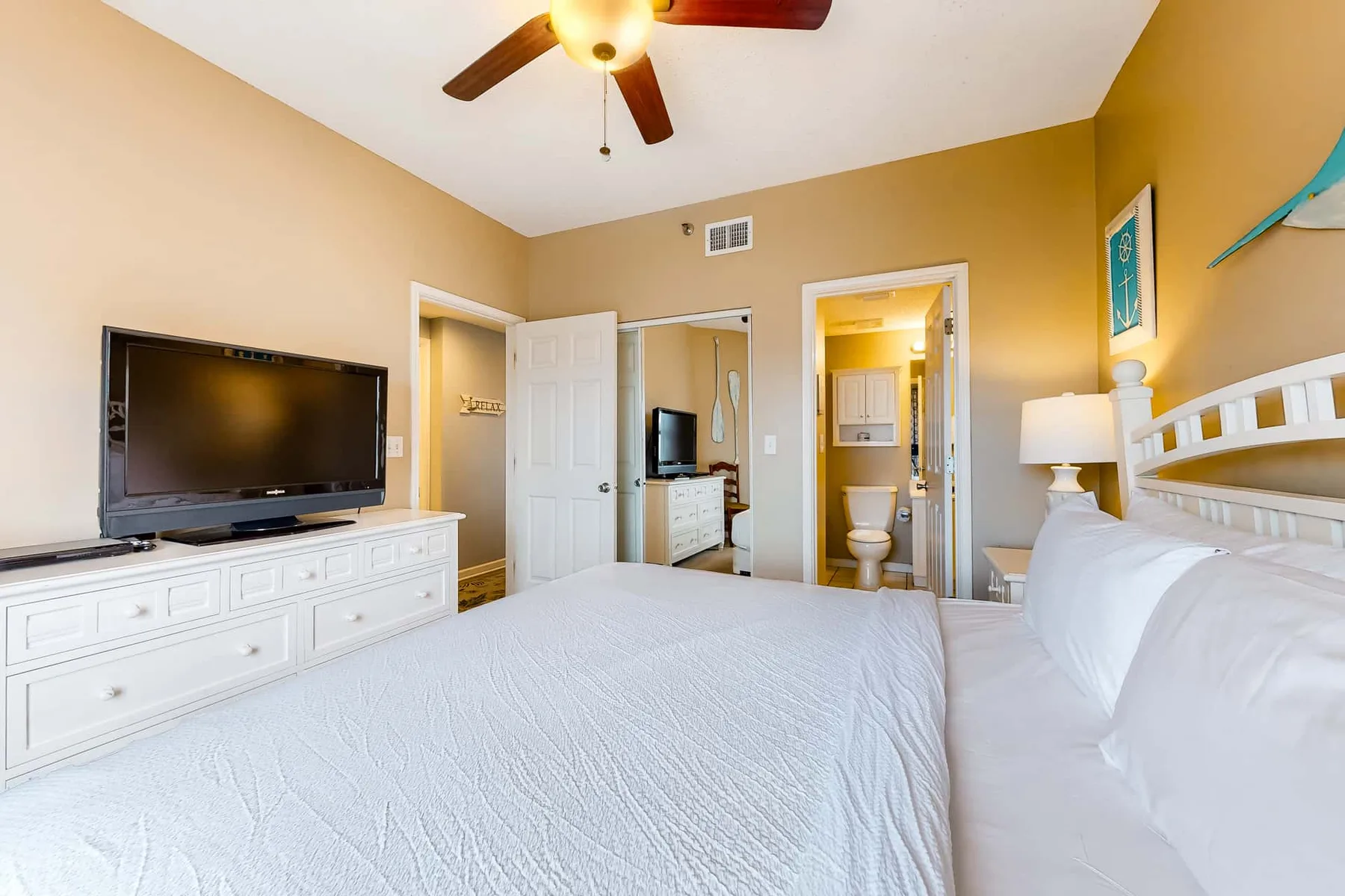 A bedroom with a large bed, television, and open doorways to adjoining spaces.