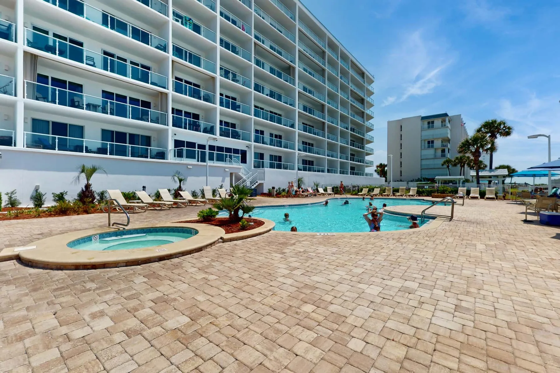 An outdoor swimming pool and round spa sit beside a multi-story building.