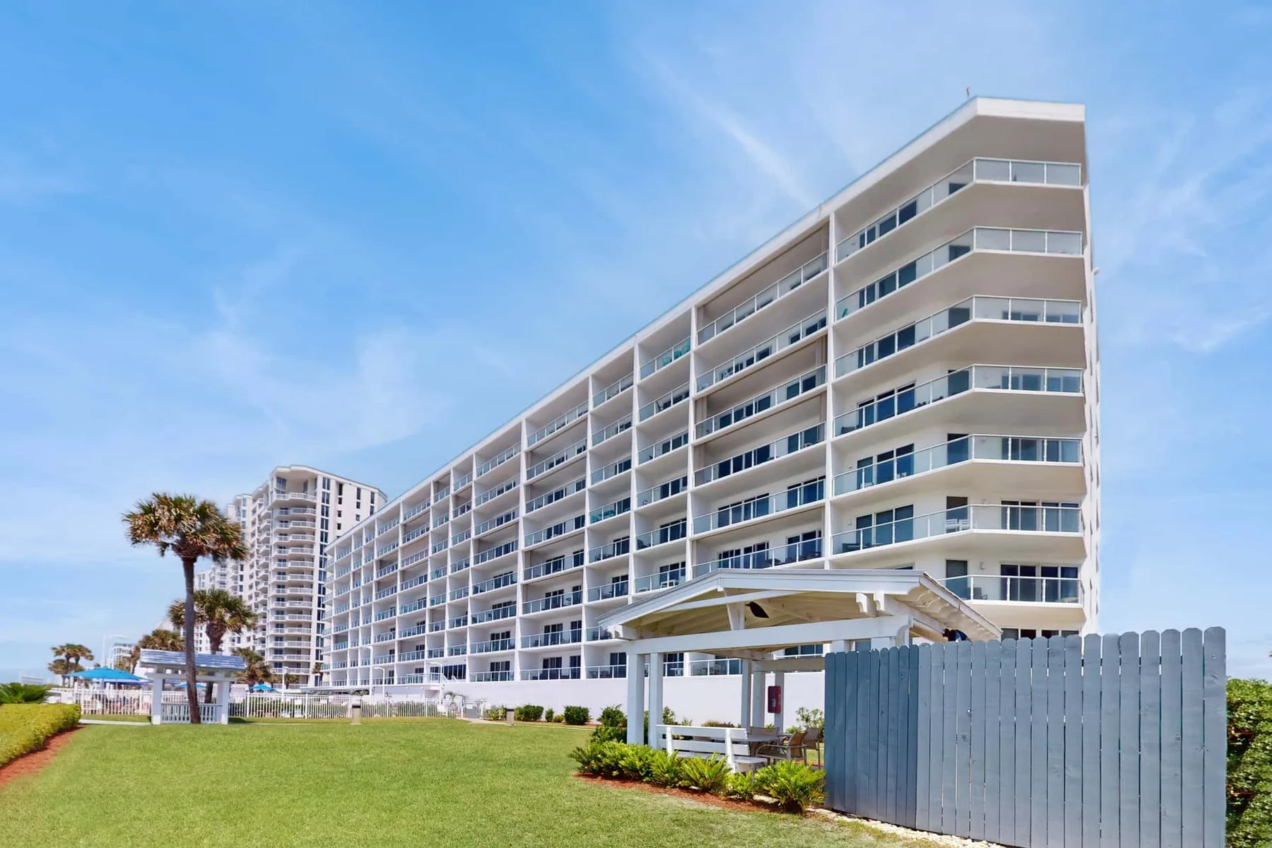 A large beachfront-style building stands beside a lawn under a blue sky.