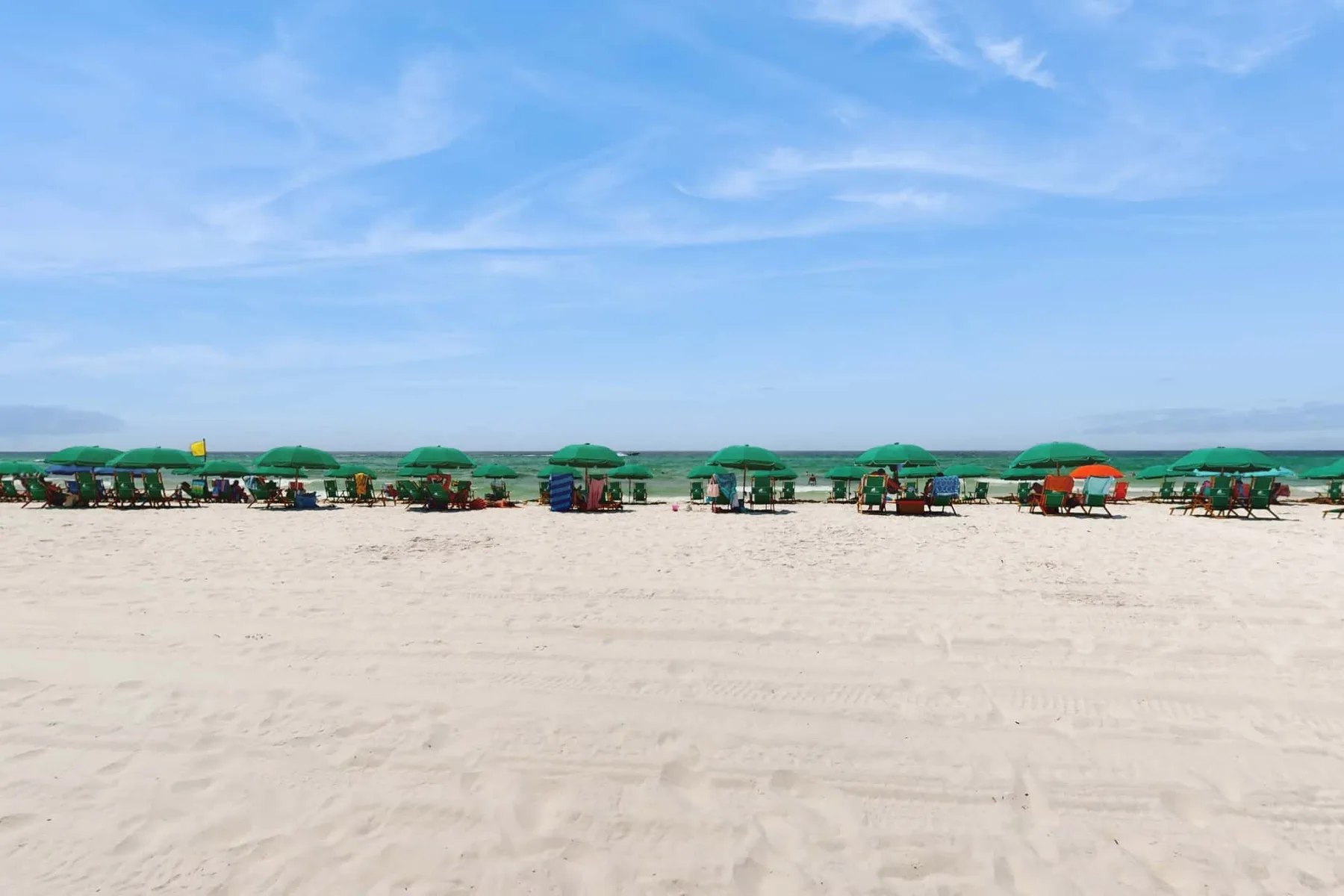 A sandy beach with rows of green umbrellas beneath a blue sky.