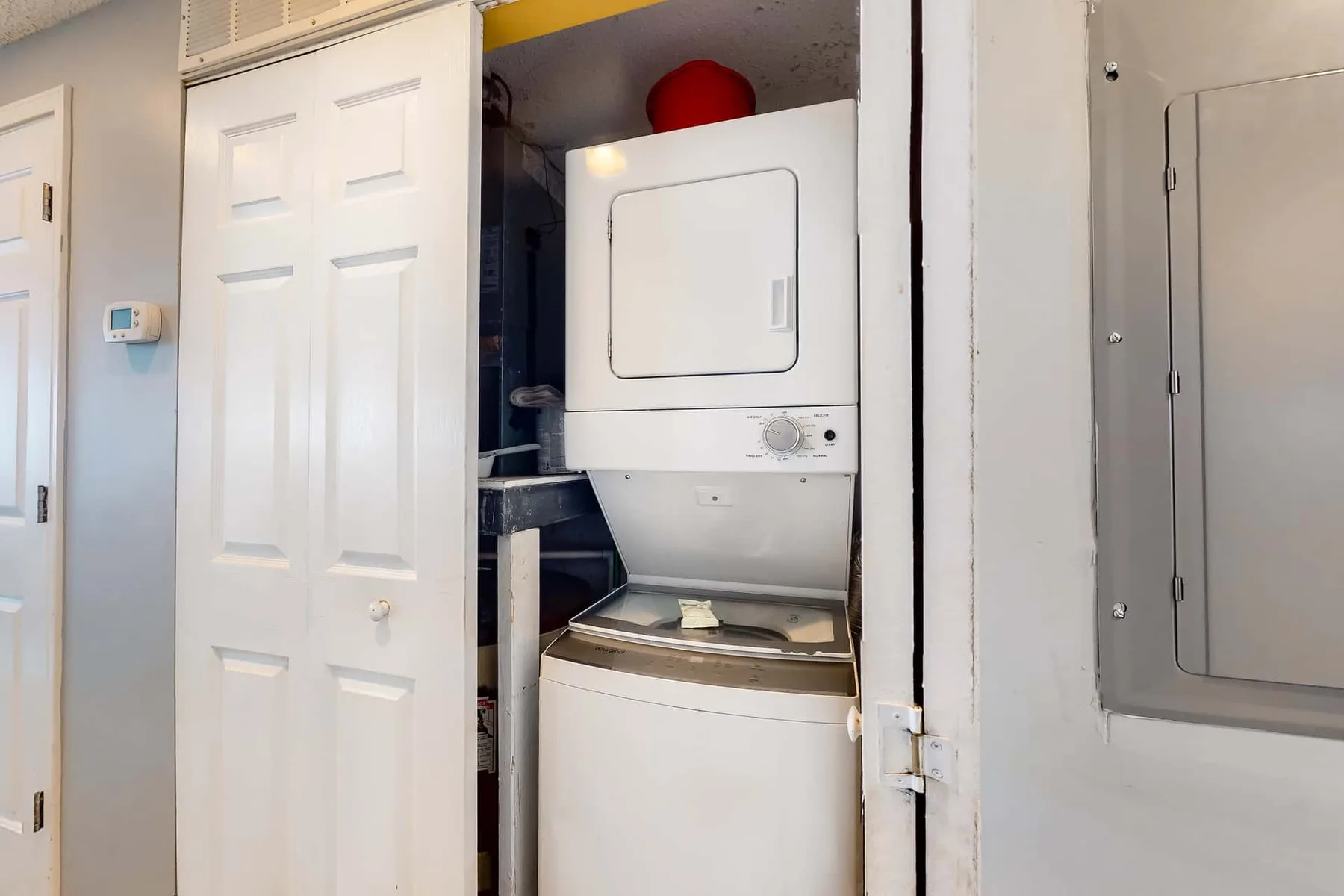 A laundry area with a stacked washer and dryer behind an open closet door.