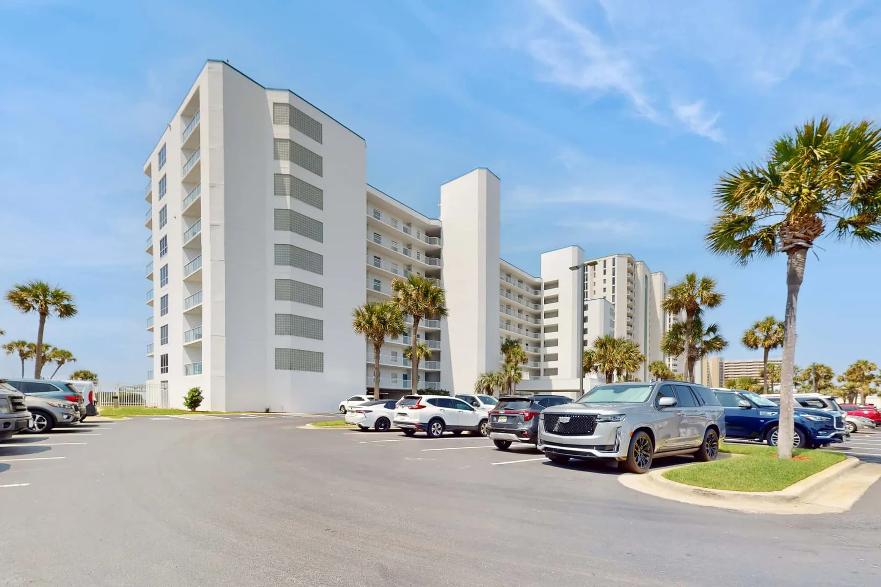 A multi-story building stands beside a parking lot lined with palm trees.