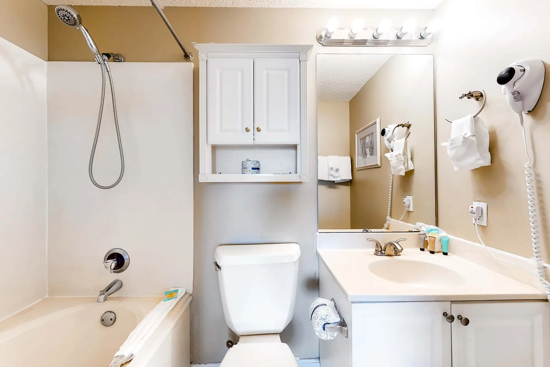 A bathroom with a bathtub, toilet, and sink beneath a wall mirror.