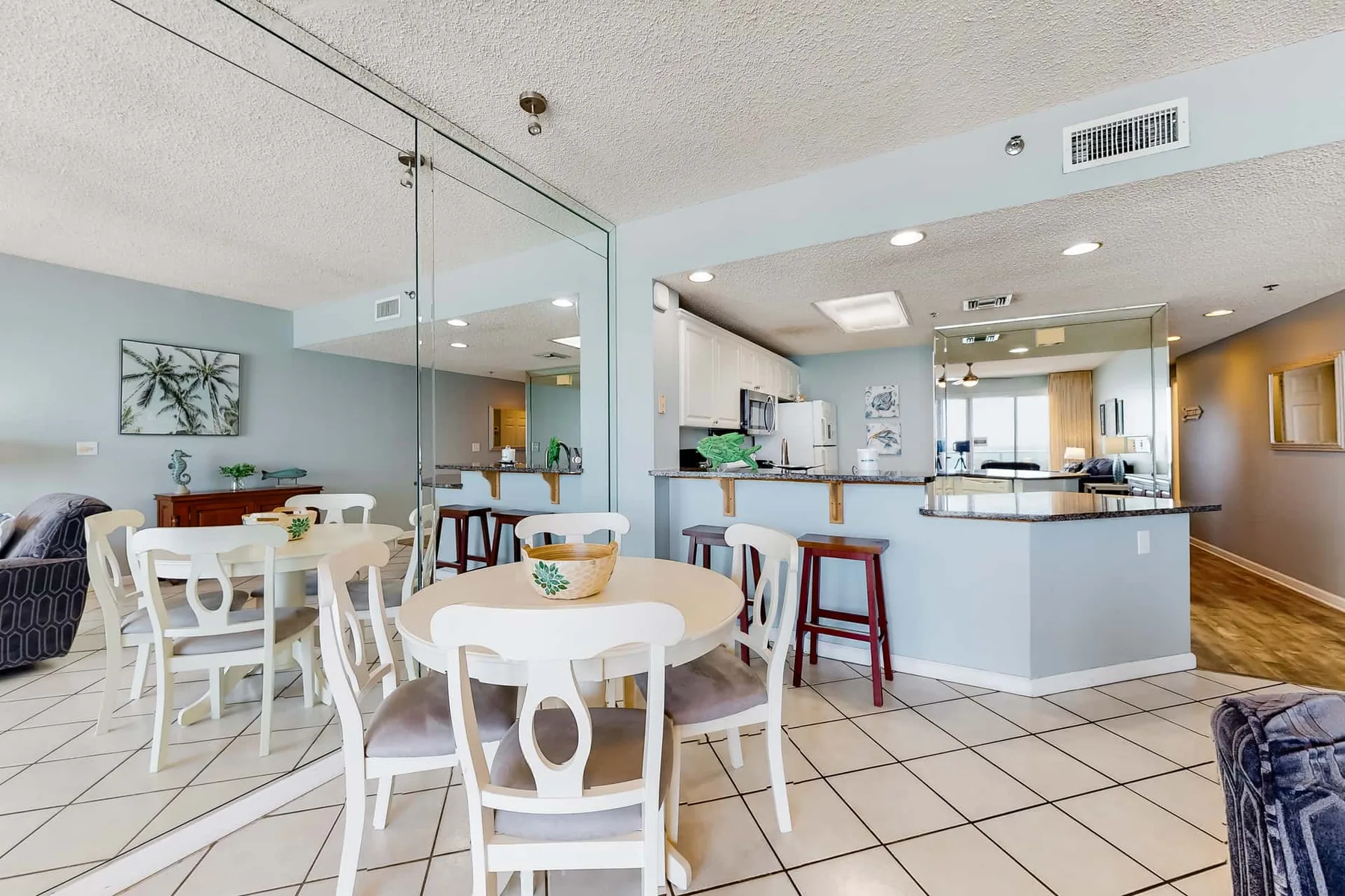 A dining area with white tables and chairs beside an open kitchen.