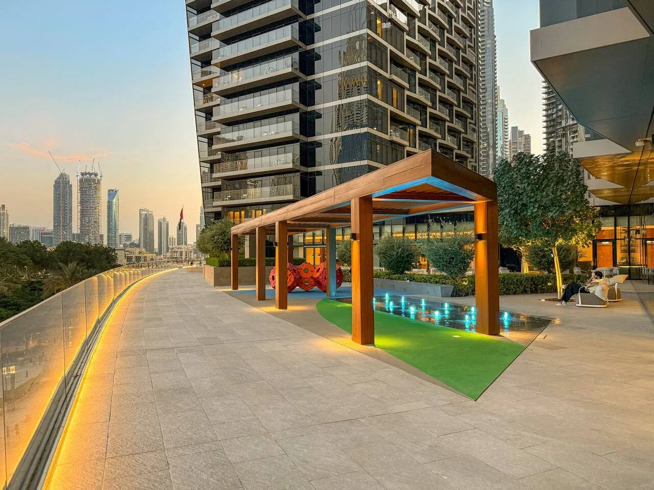 A rooftop recreation area has a swimming pool, a shaded play structure, and surrounding high-rises.