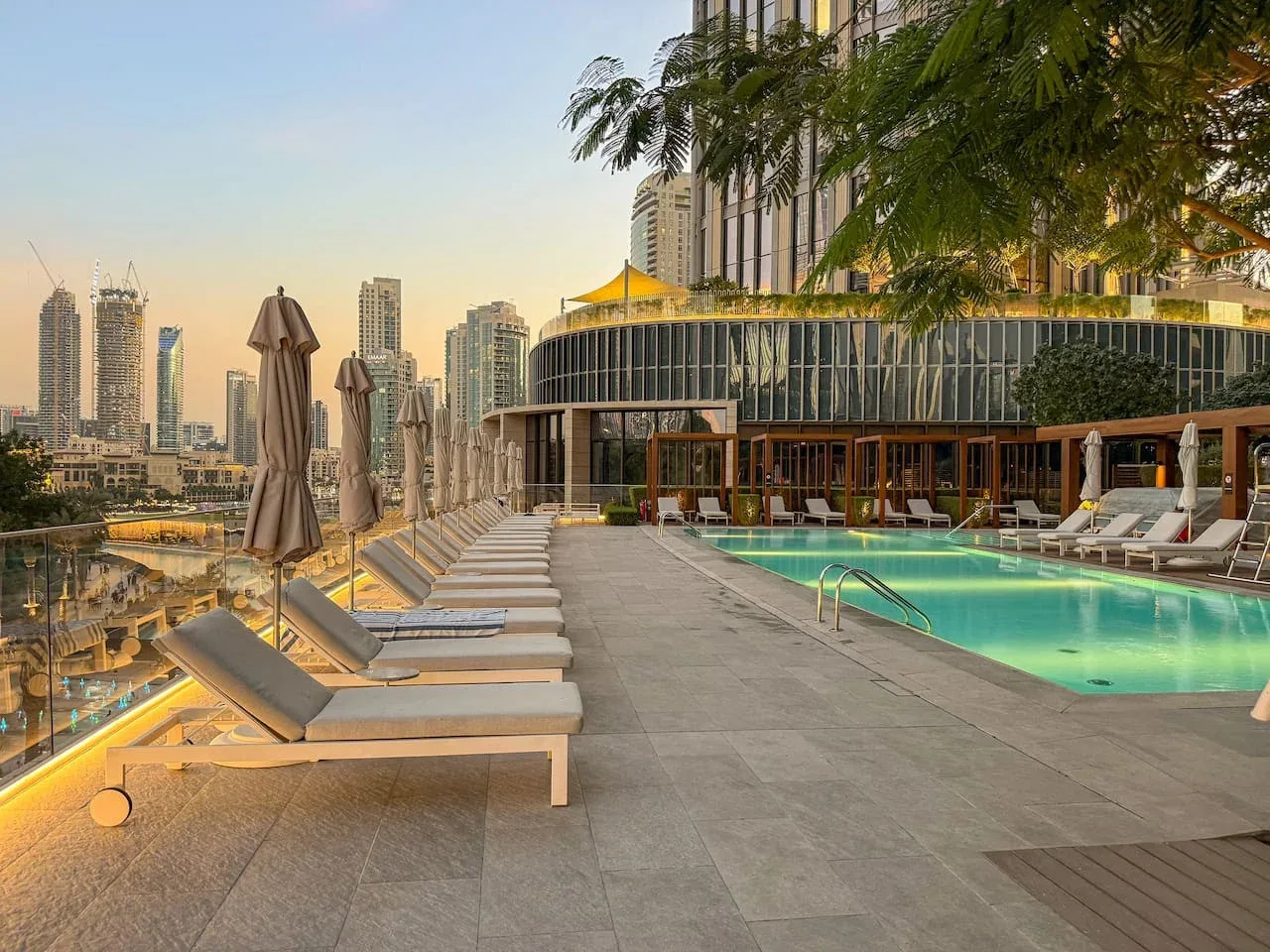 A rooftop pool deck with lounge seating overlooks a city skyline.