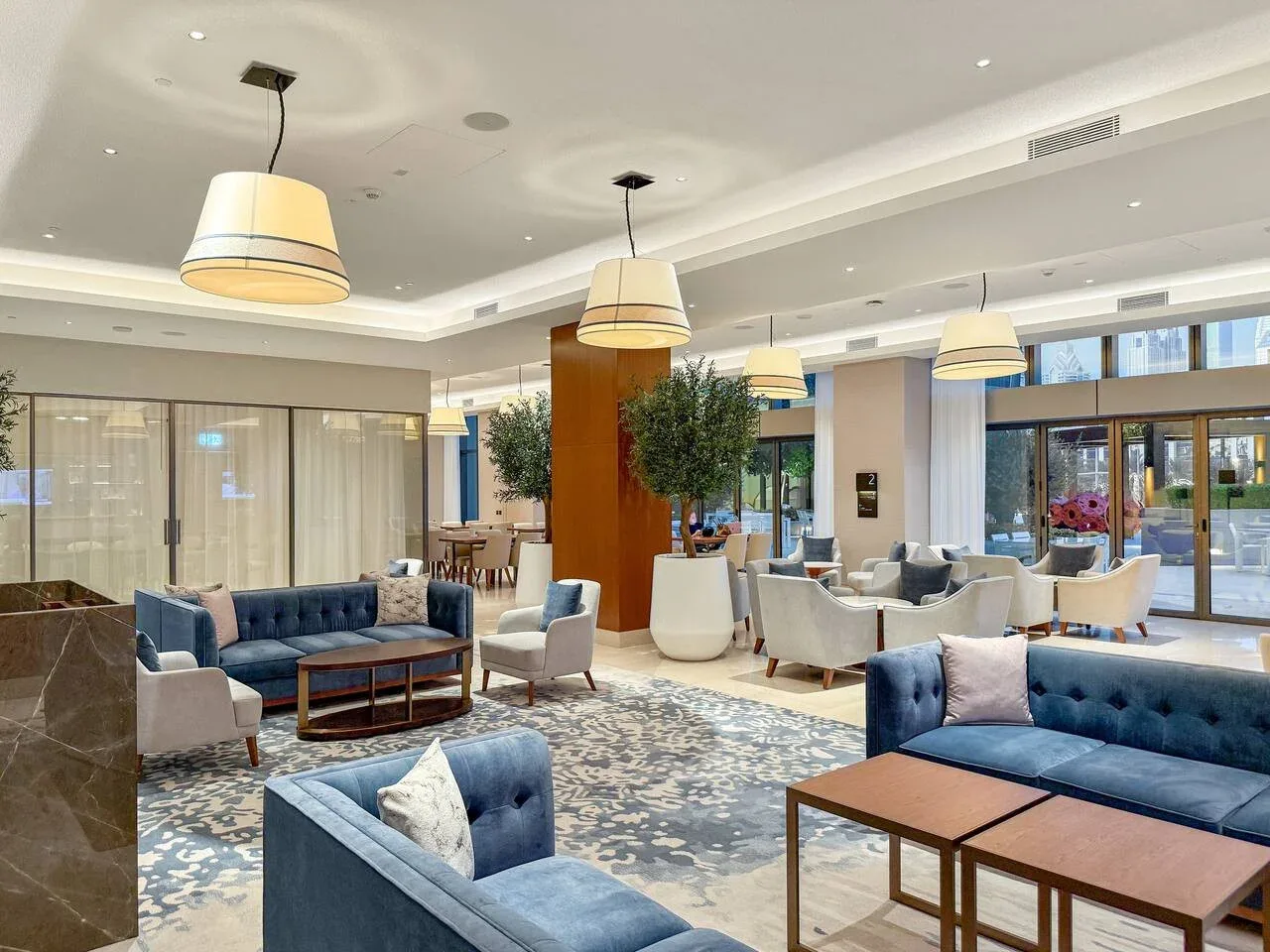 A spacious lounge with blue seating, low tables, and large windows.