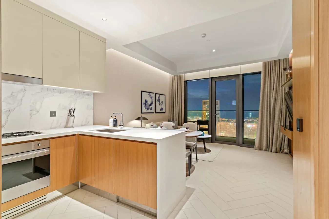 A modern kitchen with a central island opens onto a dining area and large windows.