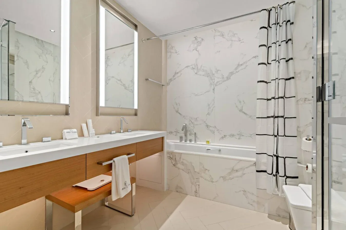 A bright bathroom with a long vanity, bathtub, and patterned shower curtain.
