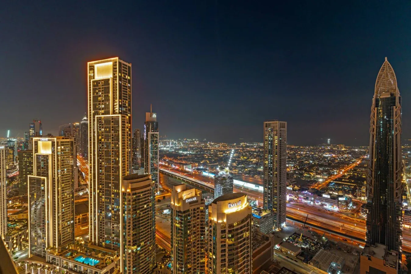 A nighttime city skyline with illuminated skyscrapers and busy roads.