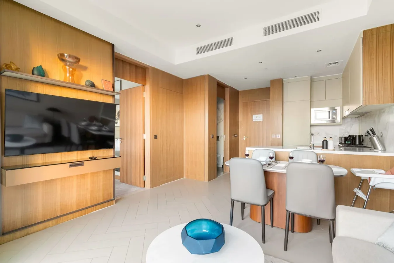 A bright open-plan room with a dining area and a television mounted on wood paneling.