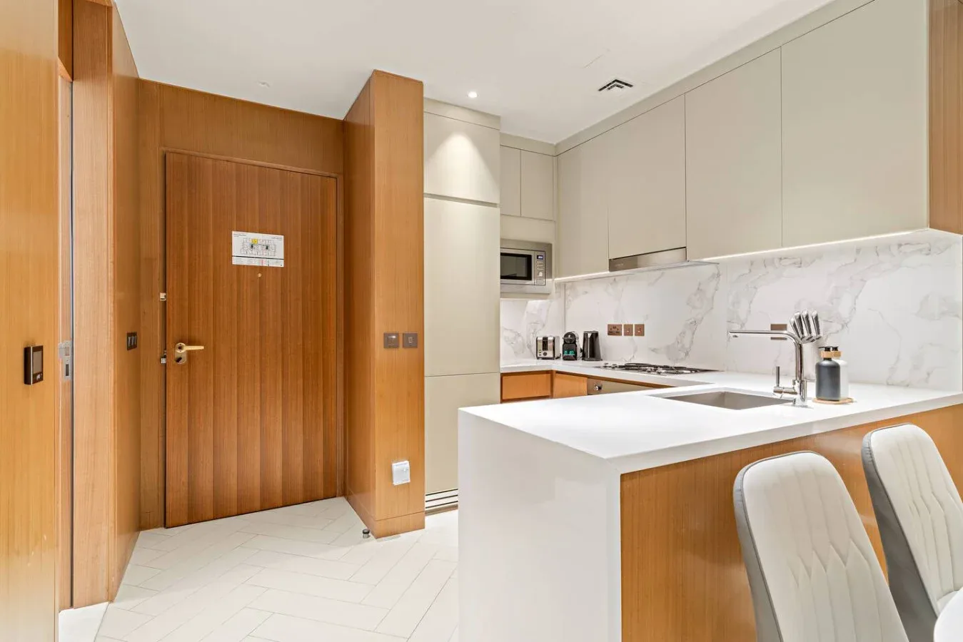 A modern kitchen with a white island, wooden cabinetry, and bar seating.