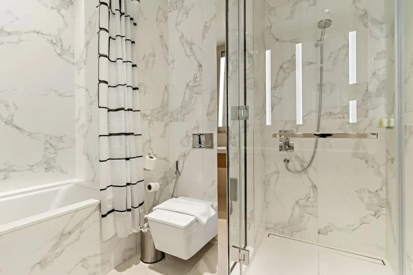 A marble-tiled bathroom with a glass shower and wall-mounted toilet.