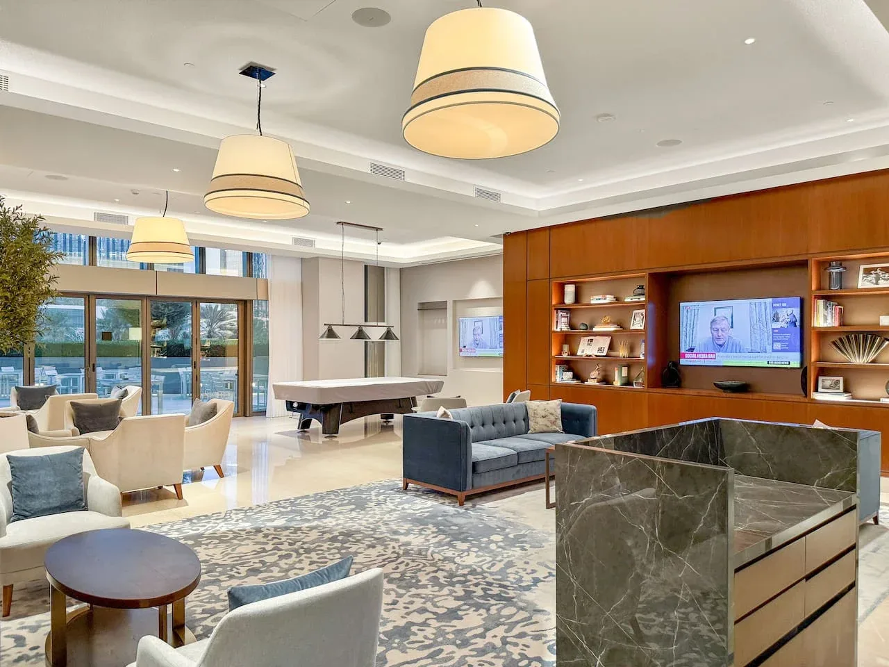 A bright living room with seating, a large rug, and a television set into a wood-paneled wall.
