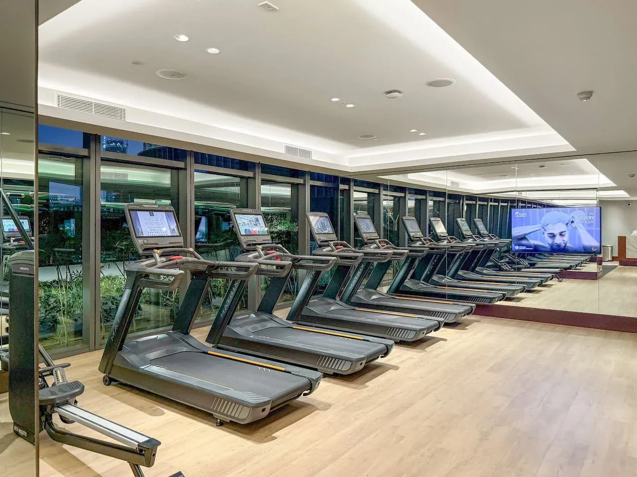 A fitness room with treadmills lined up beside large windows.