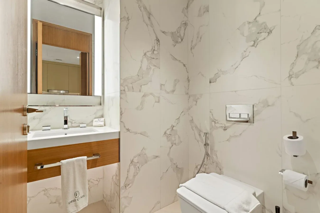 A bathroom with a marble-patterned wall, vanity, and folded towels.