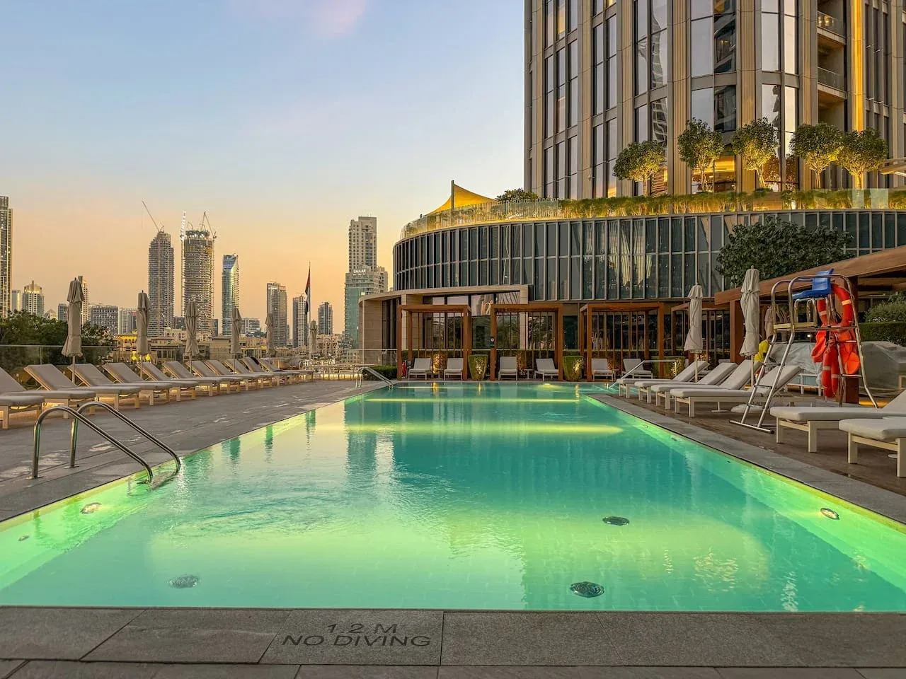 A rooftop swimming pool overlooks a city skyline at sunset.