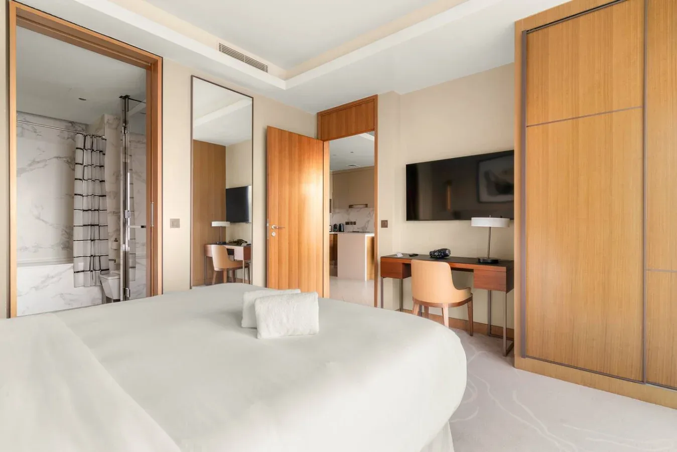A bedroom with a bed, a wall-mounted television, and a bathroom visible through an open doorway.