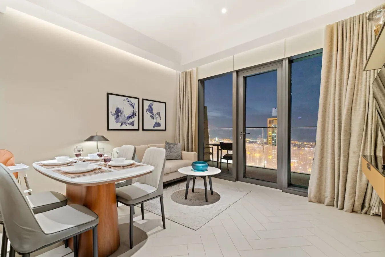 A dining and seating area beside large windows overlooking city lights.